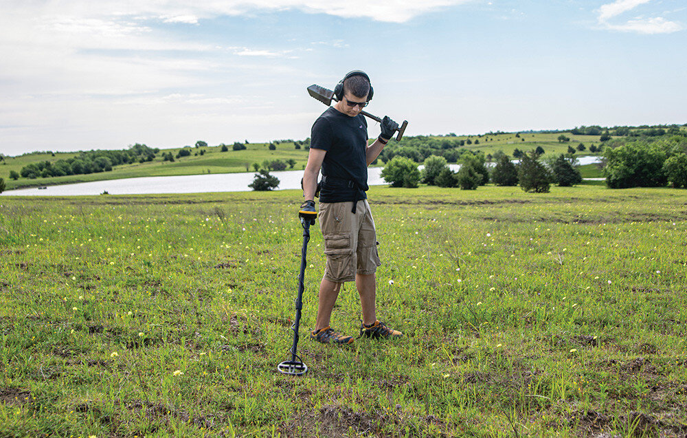 Wykrywacz metalu GARRETT ACE Apex, plaża, mineralizacja, Z-Lynk, akumulator, Poszukiwacz z wykrywaczem i łopatą na zielonej łące.