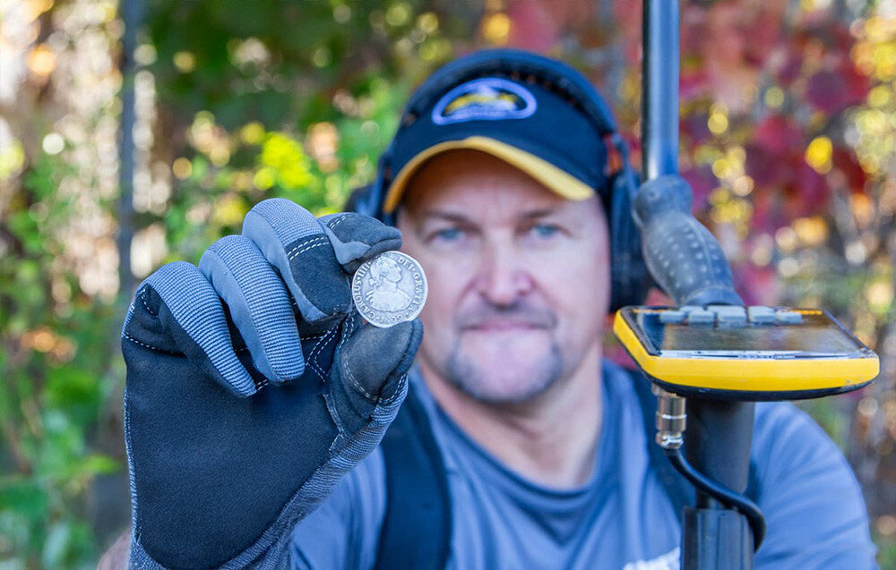 Wykrywacz metalu GARRETT ACE Apex, częstotliwości, 5kHz, 20kHz, Multi-Salt, Mężczyzna prezentuje znalezioną starą srebrną monetę.