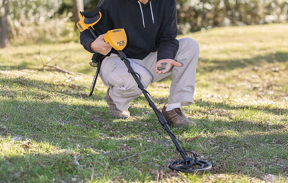 Wykrywacz metalu GARRETT ACE 300i, ACE 300i, początkujący, teren, intuicyjne, Osoba klęcząca na trawie z dłonią pełną znalezionych monet.