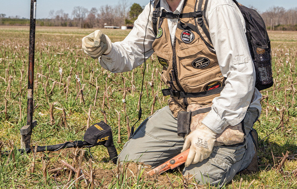 Wykrywacz metalu GARRETT ACE 400i, częstotliwość, zakłócenia, stabilna, grupowe, Klęczący poszukiwacz pokazuje monetę znalezioną na polu.