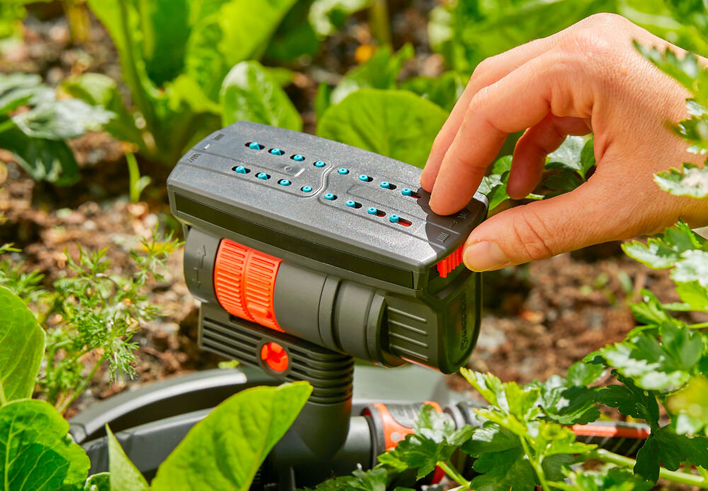Zraszacz wahadłowy GARDENA Aquazoom Compact ogród rabata warzywna osoba przesuwa palcem po suwaku na zraszaczu suwak do precyzyjnego ustawienia zasięgu od 3 do 18 metrów i szerokości strumienia od 3 do 12 metrów optymalny rozkład wody efektywne nawodnienie