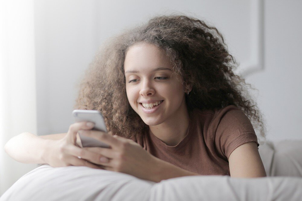 Router MERCUSYS MR50G Młoda kobieta z kręconymi włosami uśmiecha się, patrząc na ekran smartfona, leżąc na kanapie, zabezpieczenia, narzędzia