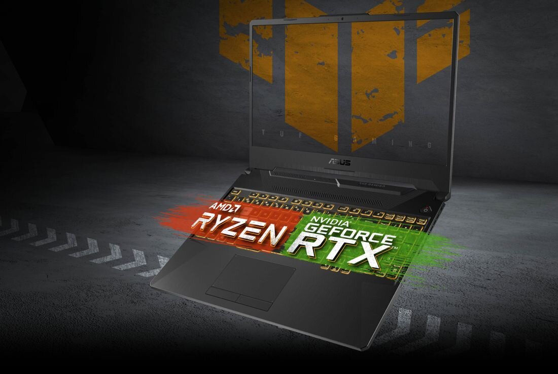 Laptop ASUS TUF Gaming A15 otwarty na tle szarej, industrialnej ściany z pomarańczowym logo TUF, na ekranie widoczne logo ASUS, a nad klawiaturą dynamiczna grafika z napisami „AMD Ryzen” i „NVIDIA GeForce RTX” w kolorach czerwonym i zielonym. - Laptop gamingowy
