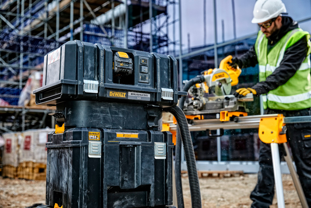 Skrzynka narzędziowa DEWALT DWST83346-1 plac budowy skrzynka ustawiona na innych skrzynkach narzędziowych obok osoba przygotowuje materiały do pracy konstrukcje porządek transport mobilność przechowywanie