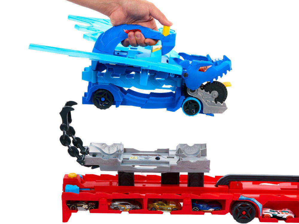 Zestaw pojazdów Hot Wheels City Transporter podwójny smok JBM72 Ręka podnosi niebieski pojazd Hot Wheels w kształcie smoka ze skrzydłami nad dużą, czerwoną lawetą, która ma miejsca parkingowe dla małych samochodzików.