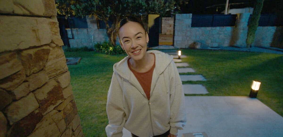 Wideodzwonek PHILIPS HUE 929003816503 Bezprzewodowy Wi-Fi Biało-czarny, światło, noc, czyste, kolorowy, Osoba w rozmytej bluzie na tle oświetlonego wieczorem ogrodu, zarejestrowana przez kamerę przy wejściu.