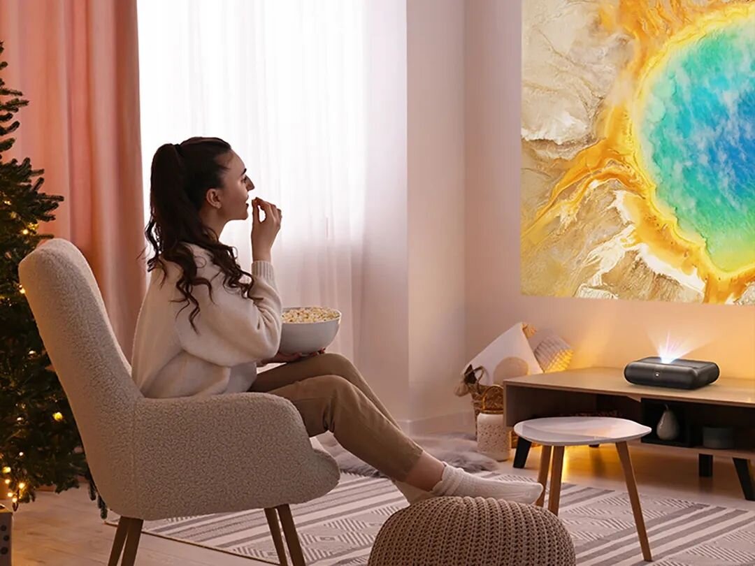 Projektor YABER K300s - Full HD, 4K i wysoki kontrast, Optyka DLP 1080p, projektor stojący na komodzie wyświetlający obraz na ścianie, osoba siedząca na fotelu