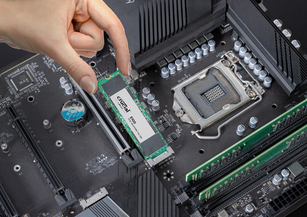 Komputer MAD DOG ENDORFY300ARGB-I06WR16WH Zbliżenie na rękę wkładającą dysk SSD M.2 marki Crucial do gniazda na płycie głównej, dysk, pojemność, interfejs, szybkość