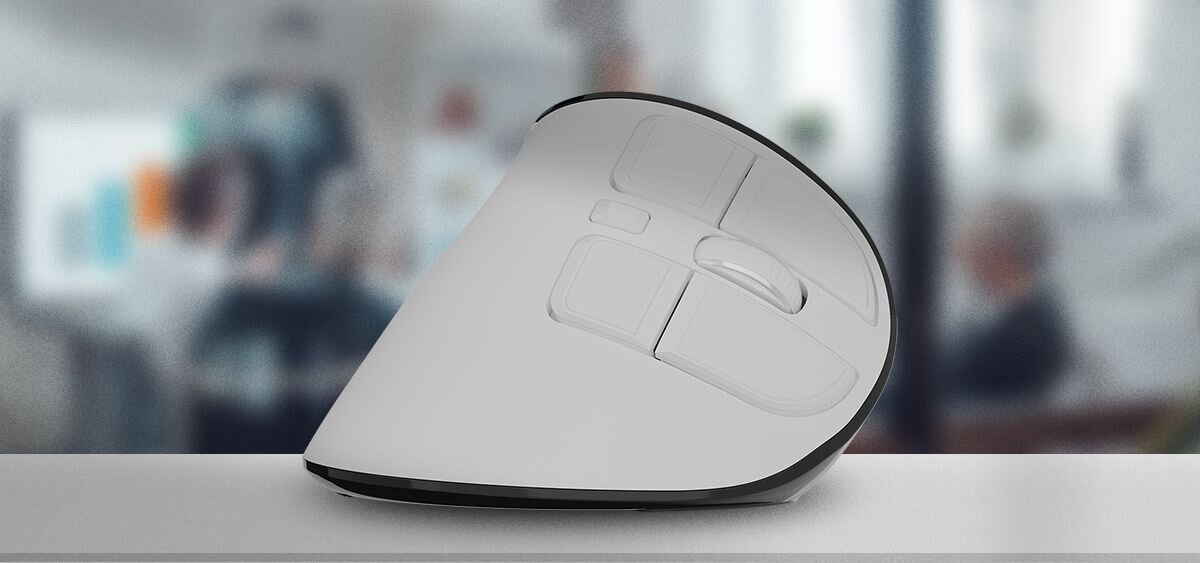 Na obrazie widoczna jest biało-czarna mysz komputerowa o ergonomicznym kształcie, umieszczona na jasnej powierzchni. W tle znajduje się rozmyty obraz wnętrza biura.