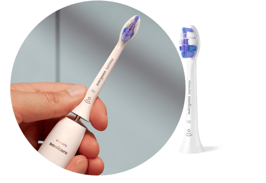 Dłoń trzymająca szczoteczkę z wyjętą końcówką. Obok znajduje się końcówka szczoteczki.