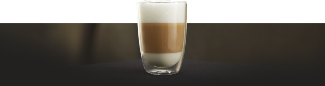 Szklanka z kawą mleczną typu latte, widoczne warstwy mleka, kawy i pianki na ciemnym tle.