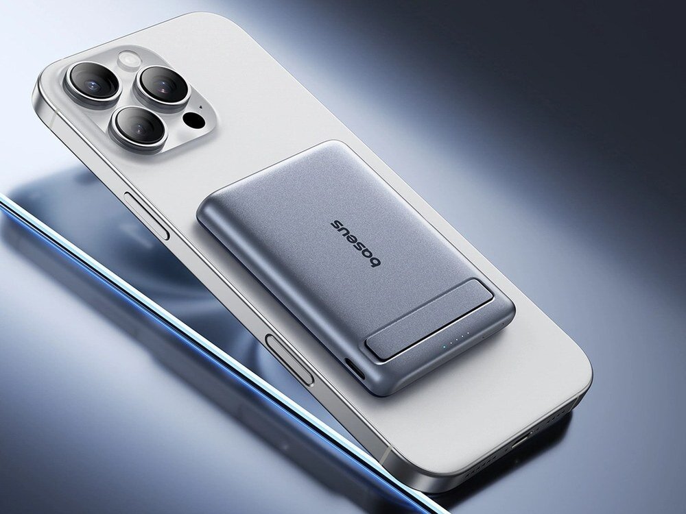 Szary powerbank Baseus z portem USB-C i wskaźnikiem naładowania leżący na białym iPhone'ie na niebieskim tle.
