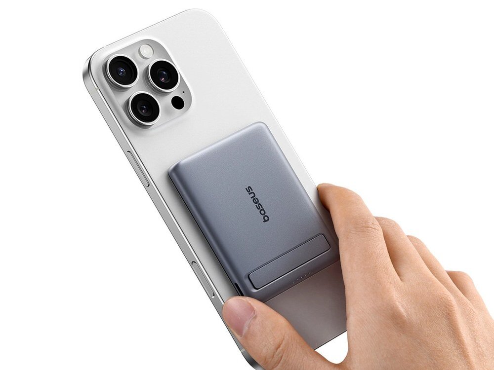 Szary powerbank Baseus z logo marki przyczepiony do tyłu białego iPhone'a trzymanego w dłoni na białym tle.