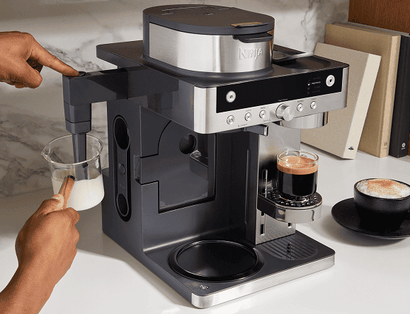 Osoba używa ekspresu Ninja CFN803EU, wkładając dzbanek z mlekiem pod dyszę spieniającą