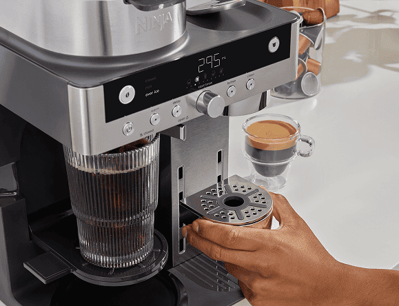 Osoba wyjmuje koszyk z filtrem z ekspresu Ninja. Widoczne gotowe kawy w szklankach