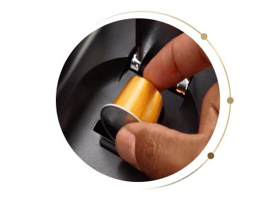 Zbliżenie na dłoń wkładającą złotą kapsułkę do gniazda w ekspresie Ninja CFN803EU