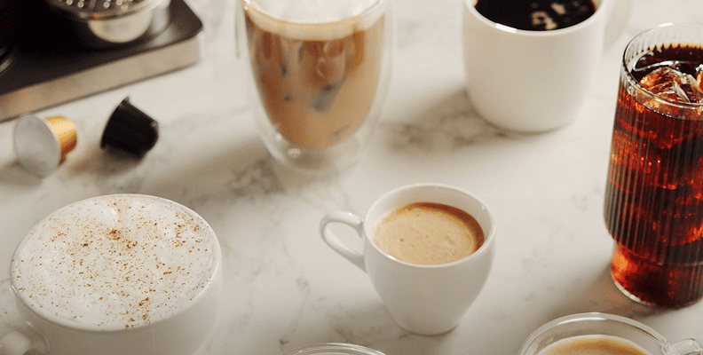 Zbliżenie na różne rodzaje kaw: spienione cappuccino, latte, cold brew i espresso na marmurowym blacie