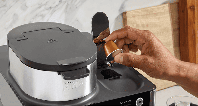 Osoba umieszcza złotą kapsułkę w ekspresie Ninja CFN803EU, widoczny panel z opcjami kawy