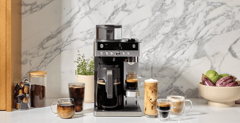 Ekspres Ninja w nowoczesnej kuchni z marmurowym blatem. Wokół różne kawy, kapsułki do ekspresu i owoce.