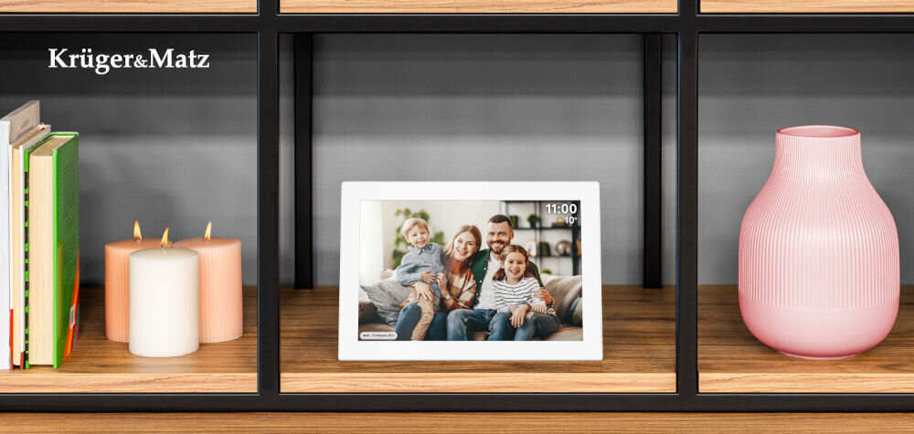 Ramka cyfrowa KRUGER&MATZ KM1100W Frameo 10.1 cala Biały prezentacja ramki ze zdjęciem i komentarzem do niej od frontu na szafce w pokoju obok świeczki książki i różowy wazon