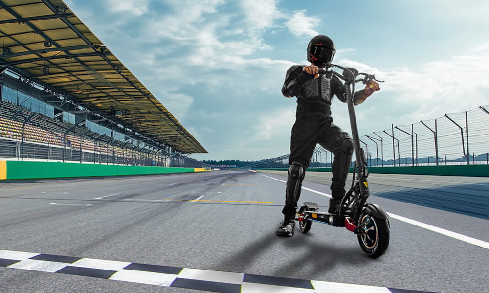 Hulajnoga elektryczna MOTUS Pro 10 Daytona 65km 2x1000W Amortyzacja 10 cali Czarny tor wyścigowy osoba stoi na ziemi jedną nogą opiera się o hulajnogę w tle niebo sygnał dźwiękowy komunikowanie się z innymi użytkownikami drogi tempomat pozwala ustawić i utrzymywać stałą prędkość pojazdu bezpieczeństwo na drodze oszczędność energii