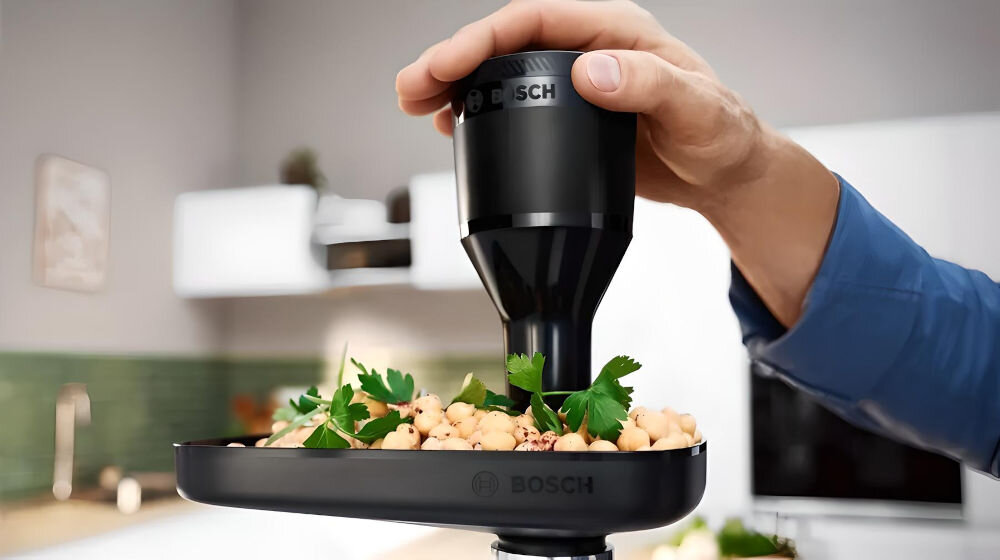 Maszynka do mięsa BOSCH MFWS642B ręka trzymająca popychacz kuchenne tło żywność wpychana do maszynki za pomocą popychacza moc przyłączeniowa 500 W imponująca moc zablokowania silnika na poziomie 2100 W twarde składniki duża moc przetwarzanie mięsa i warzyw wysoka wydajność komfort pracy w kuchni różnorodne dania  