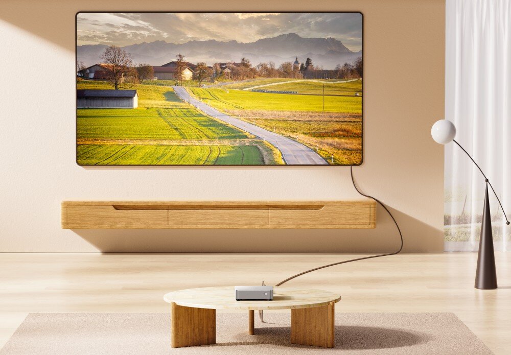 Komputer CHUWI AuBox-P-K4 Pokój dzienny z dużym ekranem wyświetlającym zdjęcie wiejskiego krajobrazu, a na niskim stoliku przed ekranem stoi mały komputer podłączony kablem, karta graficzna, obraz, rozdzielczość, jakość