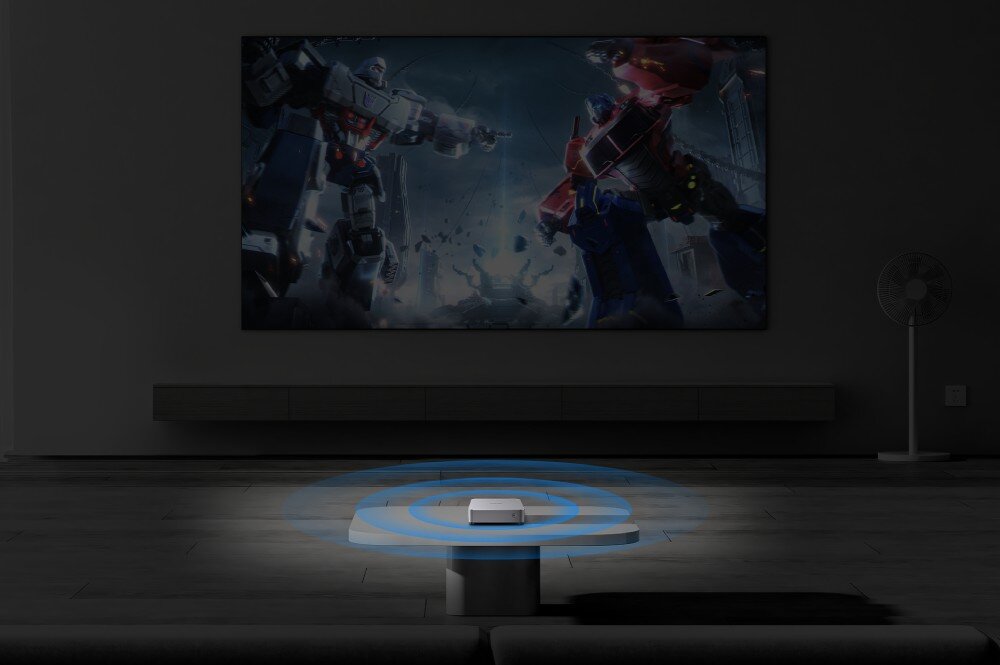 Komputer CHUWI AuBox-P-K4 Mały komputer umieszczony na stoliku w ciemnym pokoju z grafiką niebieskich fal wokół, w tle ekran z dynamiczną sceną z robotami, łączność, LAN, Wi-Fi 6, Bluetooth 5.2