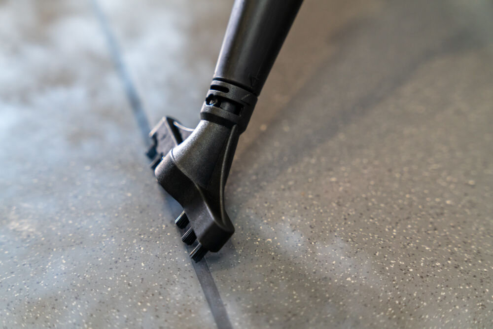 ODKURZACZ PIORĄCY SPOTCLEAN GOTZE&JENSEN CSC600 ze szczotką uniwersalną szeroką do butów do czyszczenia tapicerki meblowej samochodowej dywanów Zbliżenie na czarną końcówkę do czyszczenia fug (z podwójnymi wypustkami), która emituje parę, czyszcząc spoinę między szarymi płytkami.