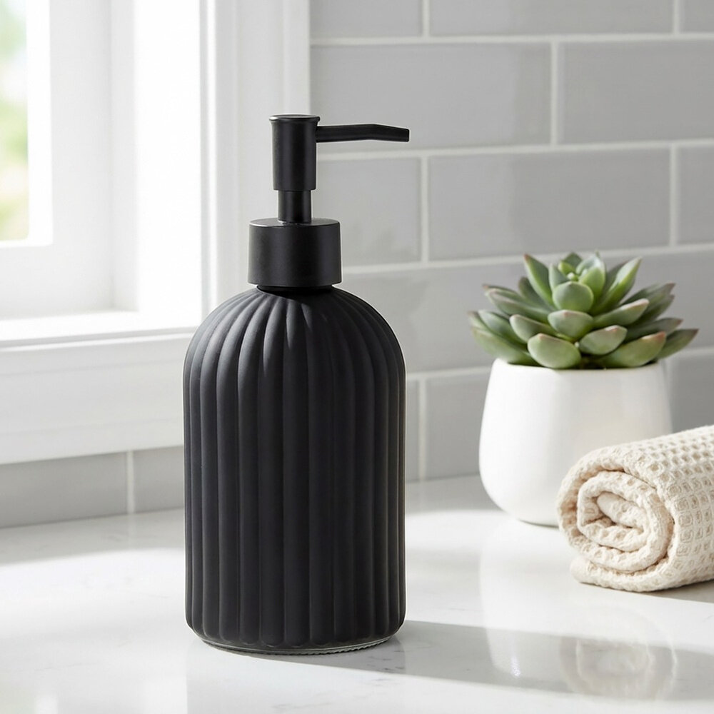 Na obrazie widoczny jest czarny, szklany dozownik do mydła o pojemności 400 ml, stojący na blacie. Obok znajduje się zwinięty ręcznik i doniczka z sukulentem, a w tle widać jasne płytki ścienne.