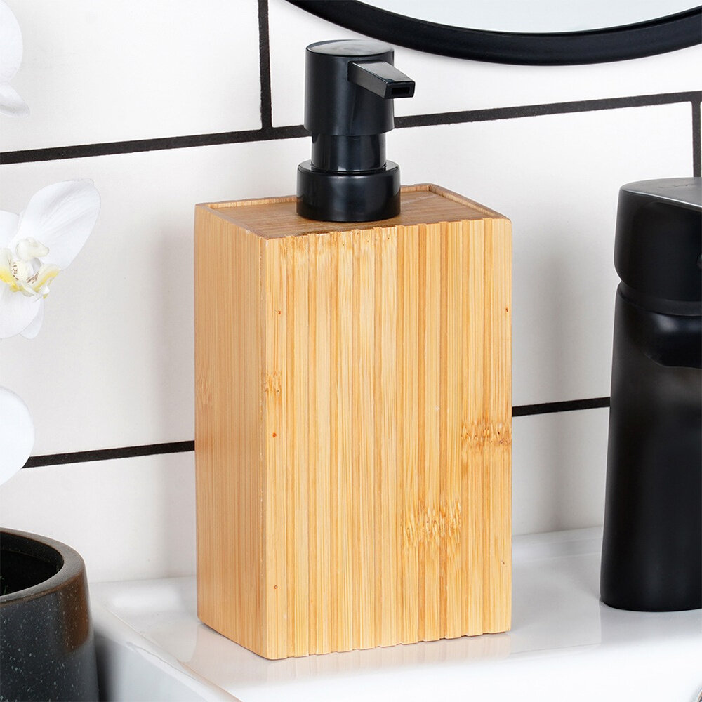 Drewniany dozownik do mydła o pojemności 280 ml z czarną pompką, ustawiony na białej powierzchni. W tle widoczne są białe płytki z czarnymi fugami oraz fragment czarnego przedmiotu.