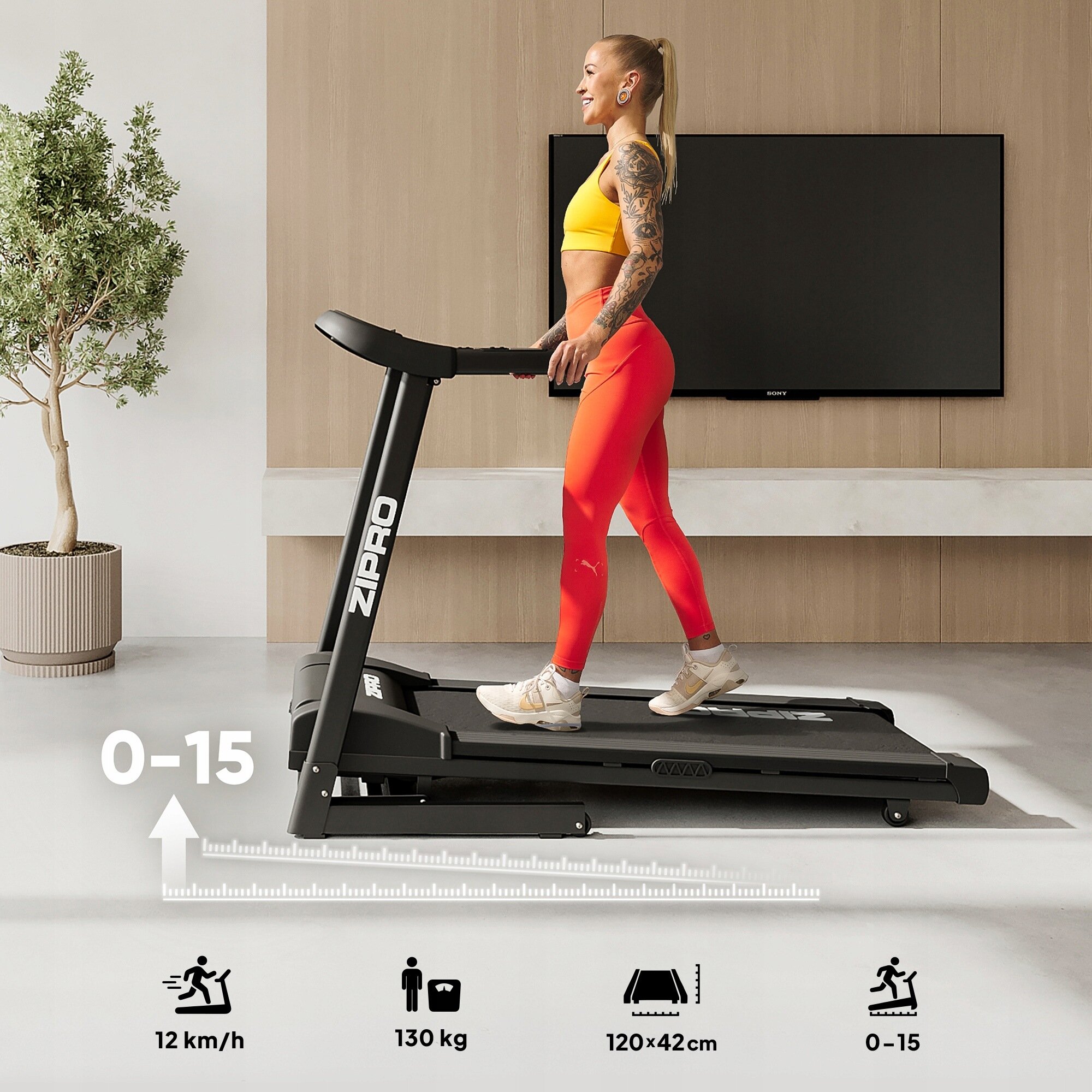 Osoba ćwiczy na bieżni Zipro w jasnym pomieszczeniu z telewizorem na ścianie i rośliną w doniczce. Na dole obrazu znajdują się ikony z informacjami: 12 km/h, 130 kg, 120x42 cm, 0-15.