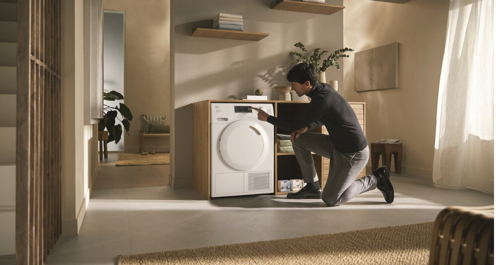 Suszarka MIELE TEA535 WP EcoSpeed zdjęcie wizualizacyjne lifestyle pomieszczenie mężczyzna zmiana ustawień panel Optymalna ochrona domu optymalne wartości szczelności ochrona domu mebli pomieszczeń