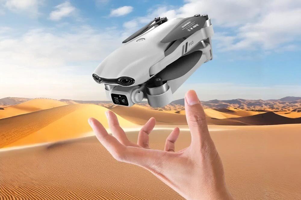 Dron EXTRALINK Smart Life F10 Zbliżenie na rękę unoszącą złożonego drona nad pustynią z piaszczystymi wydmami w tle