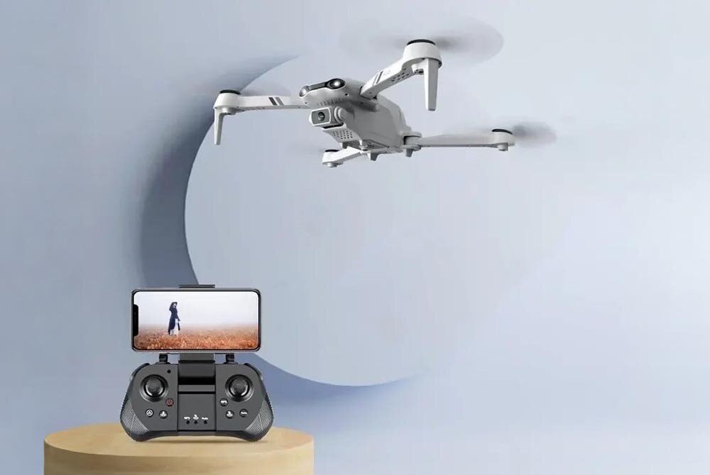 Dron EXTRALINK Smart Life F10 Dron unoszący się w powietrzu przed szarą ścianą, poniżej kontroler z zamocowanym smartfonem pokazującym obraz z kamery