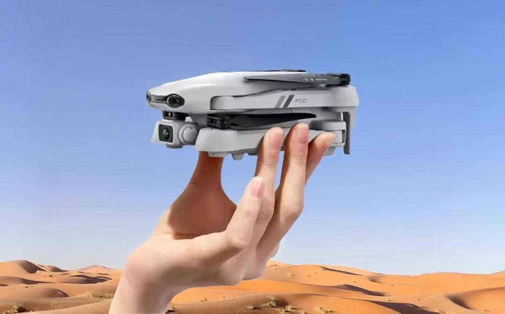 Dron EXTRALINK Smart Life F10 Ręka trzymająca złożonego drona na tle pustynnego krajobrazu i niebieskiego nieba
