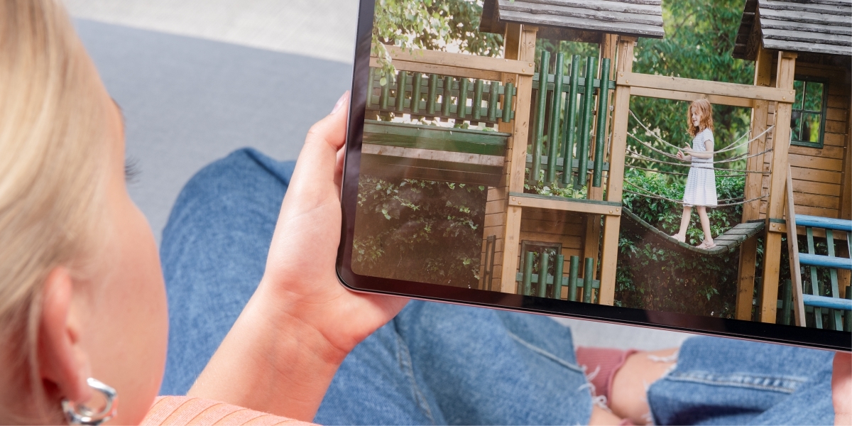 Kobieta oglądająca na tablecie obraz z kamery zewnętrznej – dziecko na drewnianym placu zabaw.