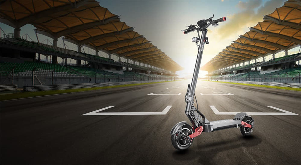 Hulajnoga elektryczna MOTUS Pro 10 Daytona 65km 2x1000W Amortyzacja 10 cali Czarny hulajnoga na tle tory wyścigowego trybuny słońće chmury do jazdy po mieście styl stabilność komfort