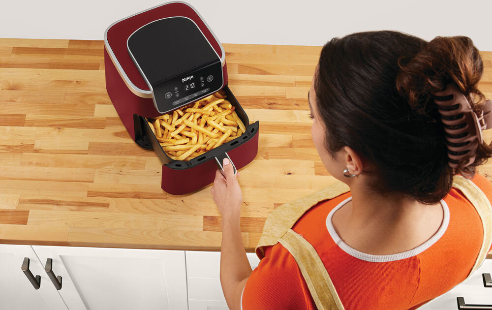 Frytkownica beztłuszczowa NINJA Foodi AF140EUCMCM Air Fryer Czerwony frytkownica stoi na blacie czerwona obudowa kobieta otwiera szufladę w szufladzie frytki jedno naciśnięcie przycisku ustawienie programu temperatury czasu działania szeroki zakres temperatur od 40 do 210 stopni delikatne podgrzanie resztek obiadu Precyzyjna regulacja temperatury optymalne efekty kulinarne 