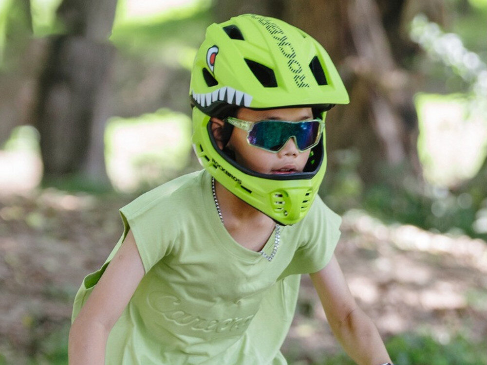 Kask rowerowy ROCKBROS TT-32004 Shark Zielony Full Face dla Dzieci z odkręcaną szczęką (rozmiar M), regulacja, dopasowanie, klamra, stabilność, Dziecko w kasku z motywem rekina patrzące przed siebie podczas jazdy na rowerze.