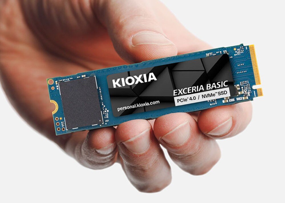 Dysk KIOXIA Exceria Basic Dłoń trzymająca poziomo wewnętrzny dysk SSD M.2 na jasnym, jednolitym tle, z widoczną czarną etykietą producenta, format, pojemność, interfejs