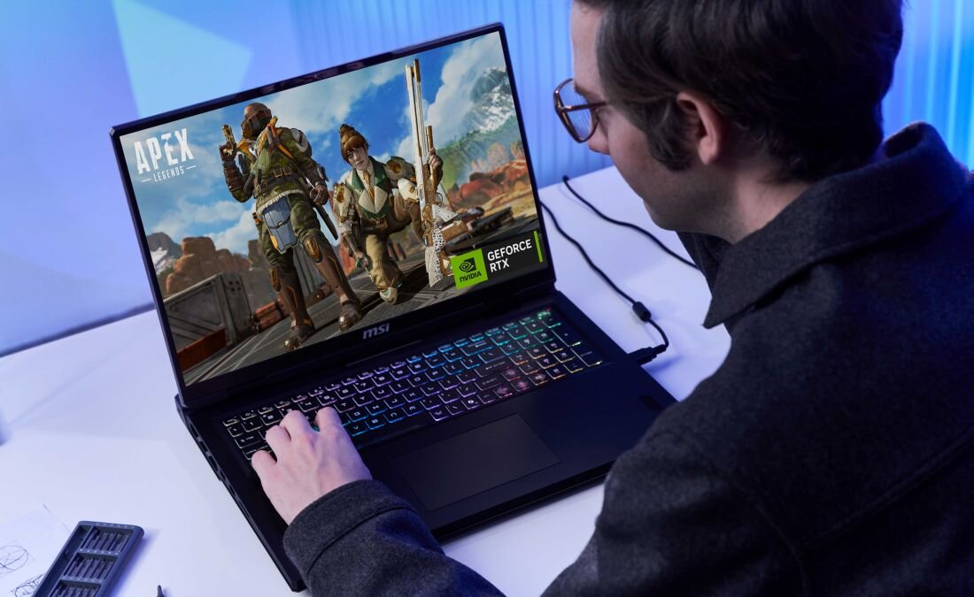 Mężczyzna w okularach gra na laptopie MSI Vector w grę „Apex Legends”; na ekranie widoczne są postacie z gry, klawiatura ma tęczowe podświetlenie, a na obudowie znajduje się naklejka GeForce RTX, co ilustruje gamingowe przeznaczenie komputera. - GeForce RTX, NVIDIA Blackwell, NVIDIA DLSS 4