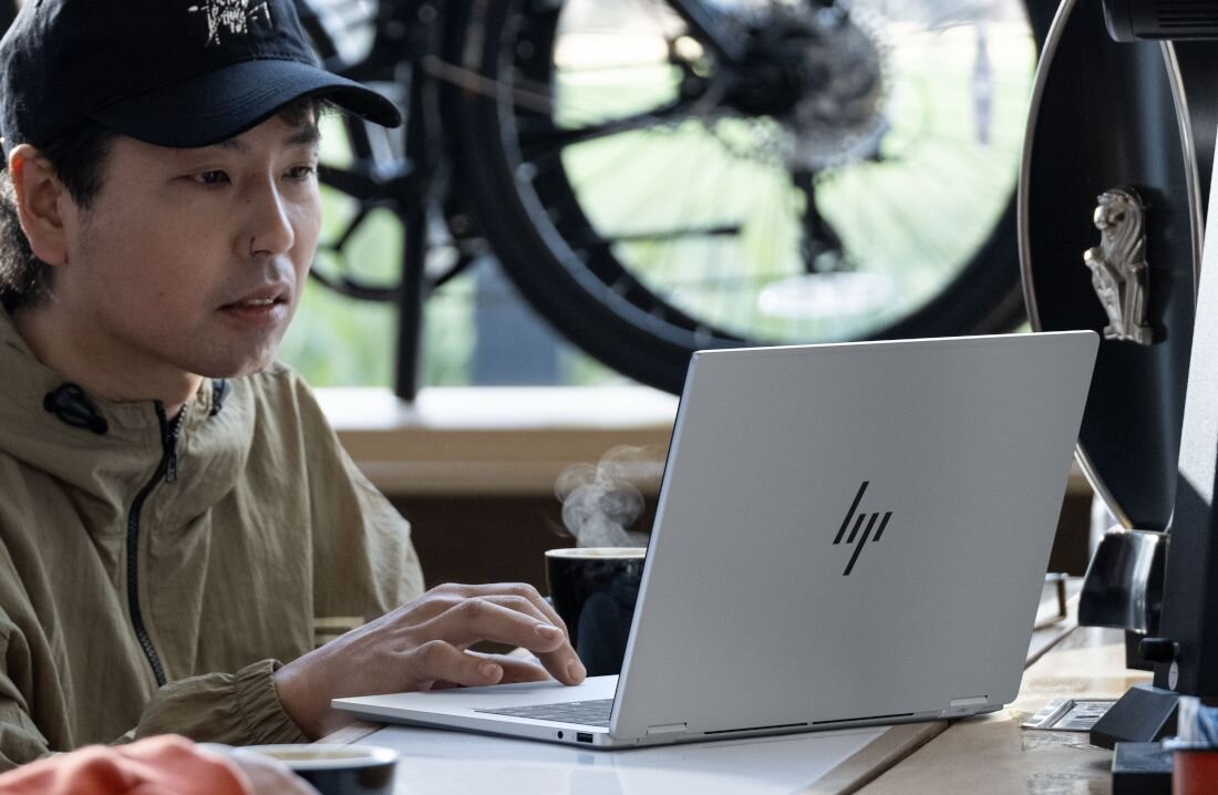 Praca na srebrnym laptopie HP OmniBook w kawiarni, rower widoczny w tle na stojaku.