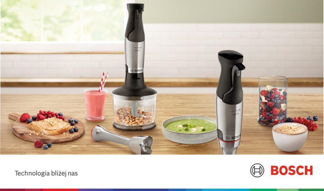 Na drewnianym blacie kuchennym znajduje się blender ręczny z logo BOSCH, obok którego leżą różne potrawy, takie jak smoothie, zupa i owoce. Na dole obrazu widnieje napis \'Technologia bliżej nas\' oraz logo BOSCH.