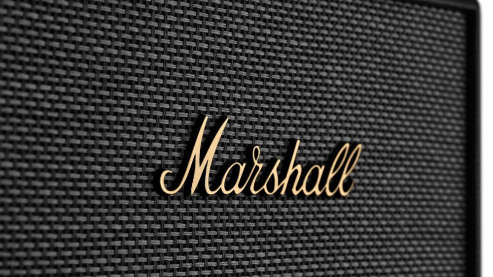 Zbliżenie na czarną kratkę głośnika z widocznym złotym logo \'Marshall\'.