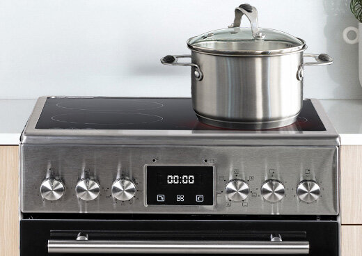 Zbliżenia na płytę ceramiczną i pokrętła kuchenki elektrycznej MPM-55-KEC-40. Na płycie garnek z pokrywką.