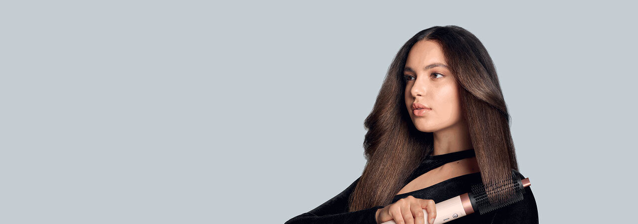Modelka o brązowych włosach modeluje końcówki używając multistylera Dyson Airwrap Coanda2x.