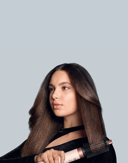 Modelka o brązowych włosach modeluje końcówki używając multistylera Dyson Airwrap Coanda2x. Wersja mobile.