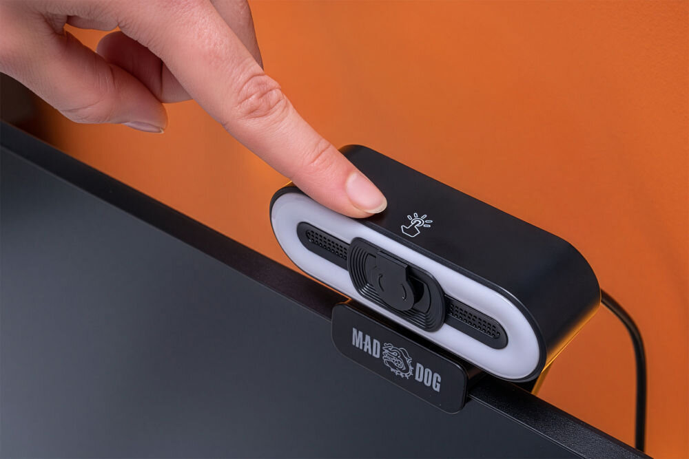 Kamera internetowa MAD DOG IC200K Ręka dotykająca dotykowego włącznika lampy LED w kamerze MAD DOG IC200K, zamontowanej na górze monitora.