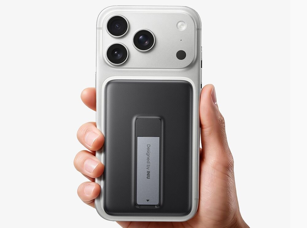 Osoba trzyma telefon z zamontowanym czarnym powerbankiem, na którym widnieje napis \'Designed by INIU\'.